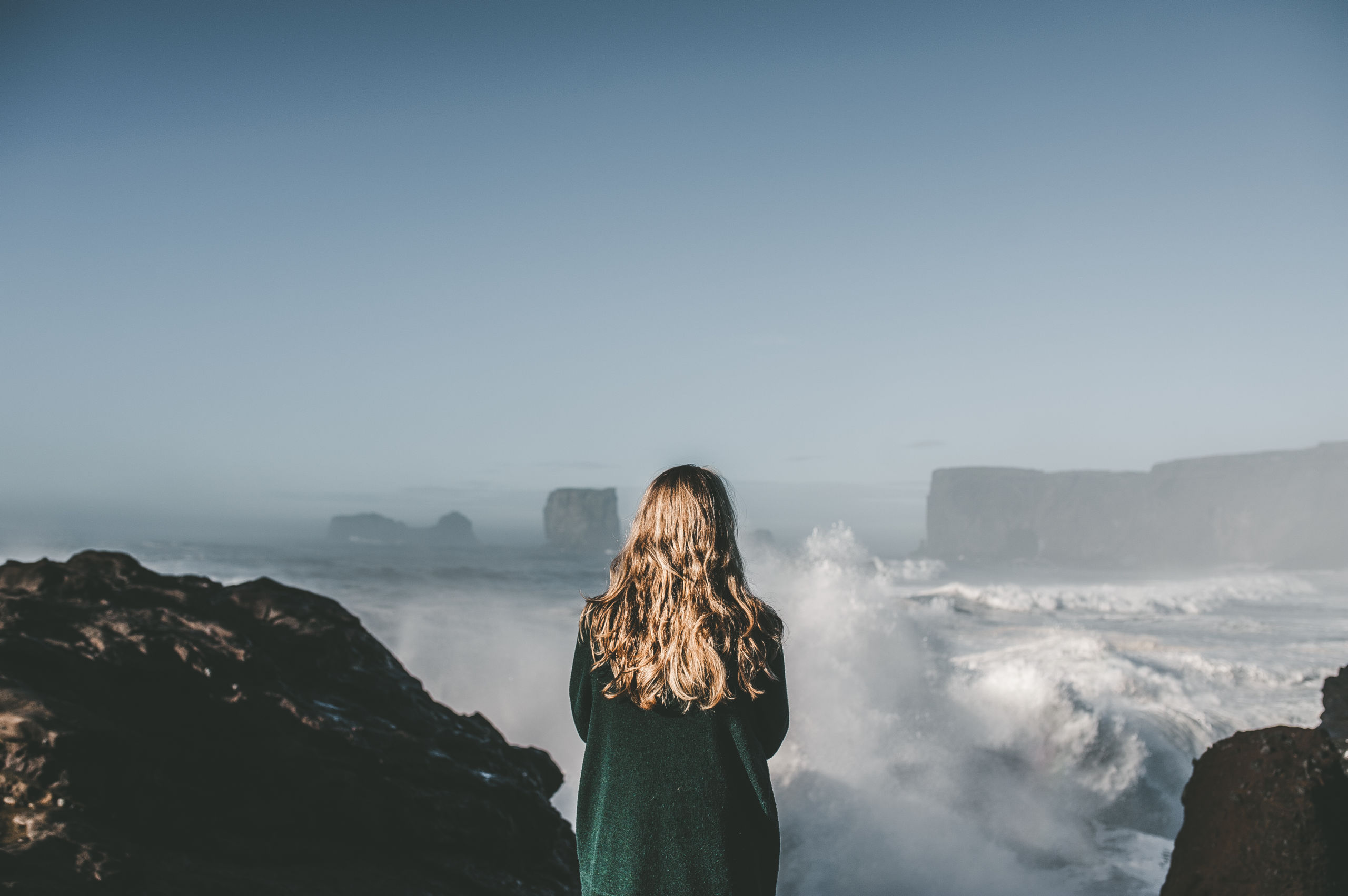 A person standing at dyrholaey sea arch overlooking the rough waters in Iceland
