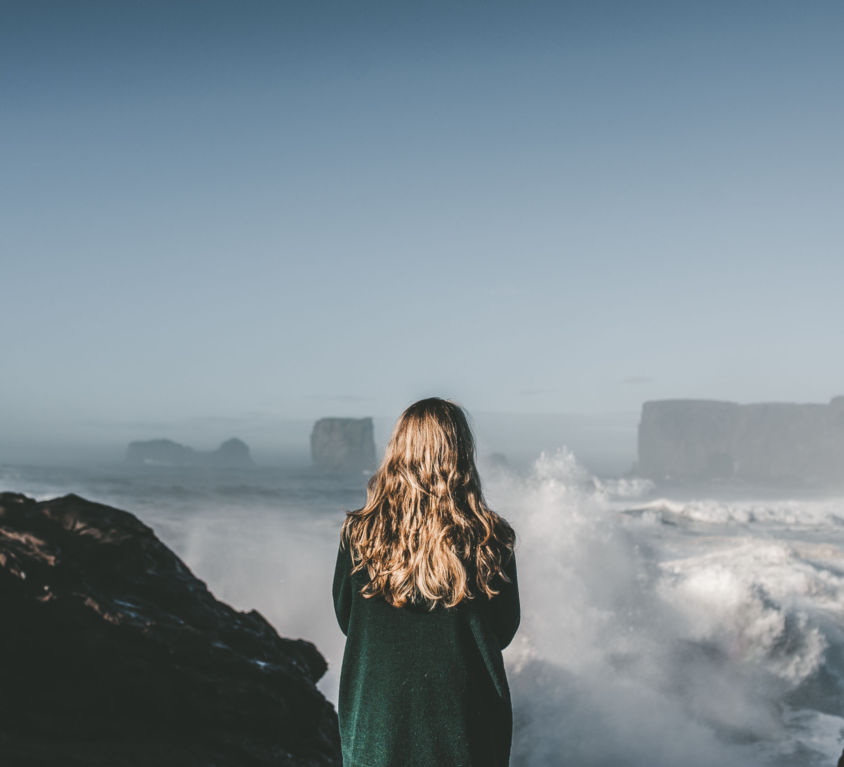 A person standing at dyrholaey sea arch overlooking the rough waters in Iceland